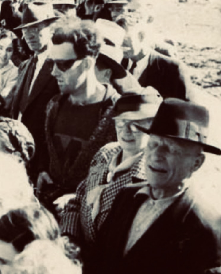 Fotografía en blanco y negro de una multitud en la década de 1940, destacando un hombre con gafas de sol oscuras, una camiseta con estampado y un suéter con cremallera. Su vestimenta moderna ha generado teorías sobre John Titor, el supuesto viajero en el tiempo.