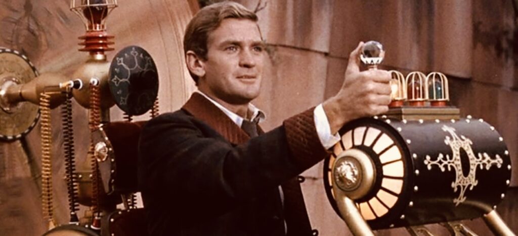 La Máquina del Tiempo-1960 Escena de la película ‘La Máquina del Tiempo’ (1960), basada en la novela de H.G. Wells. El protagonista, George, interpretado por Rod Taylor, está sentado en una máquina del tiempo de estilo steampunk, sosteniendo una palanca de cristal mientras se prepara para viajar a través de los siglos. La máquina, decorada con engranajes dorados y luces brillantes, representa un icónico diseño retrofuturista del cine clásico de ciencia ficción.